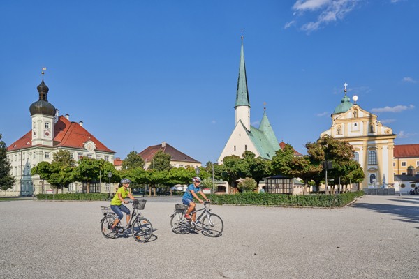 Das Foto zeigt zwei Radfahrer auf dem Stadtplatz von Altötting.