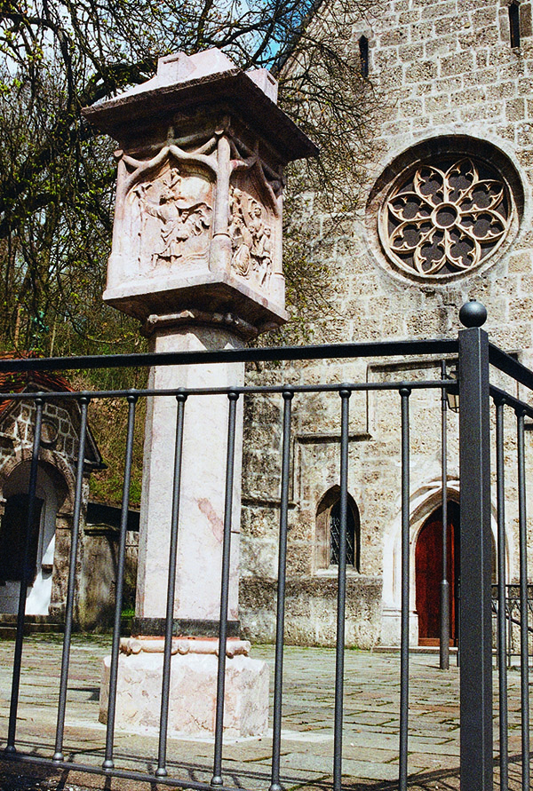 Das Foto zeigt die gotische Säule aus Stein vor der Katholischen Kirche Sankt Andreas.