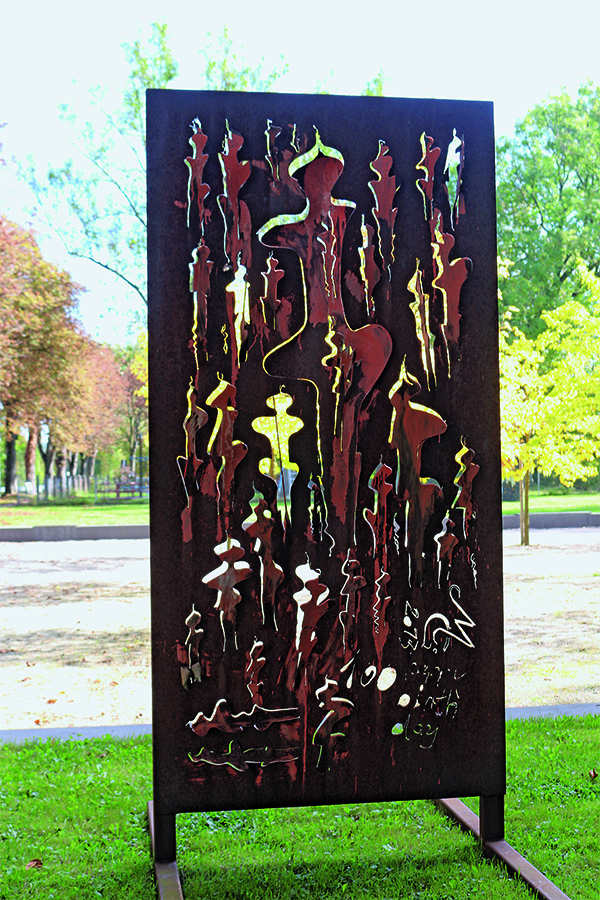 Das Foto zeigt eine senkrecht stehende Stahlplatte, aus der der Künstler verschiede Muster geschnitten hat.