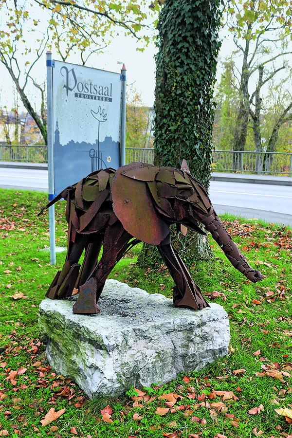 Das Foto zeigt einen kleinen, verrosten Elefanten aus Stahl auf einem Steinsockel.