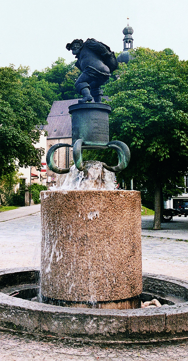 Das Foto zeigt einen Steinbrunnen, in dessen Mitte auf einer Steinsäule Hans von Pienzenau seinen nackten Hintern zeigt.