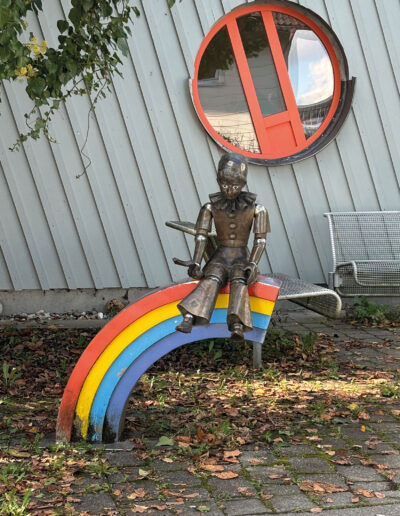 STIRNBERG, Bonifazius: „Kasperl auf Regenbogen“, 1994, Aluguss. Regenbogen-Kindergarten, Lindacher Straße 2